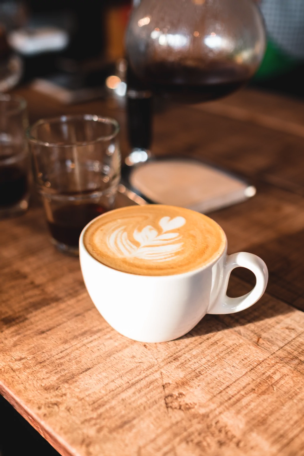 A white cup of latte with leaf-shaped art sits on a wooden table, like those enjoyed at Always Reddy Nutrition in Pittsburgh, PA—owned by Allison Reddy, dietitian for neurodivergent nutrition care. in Pennsylvania