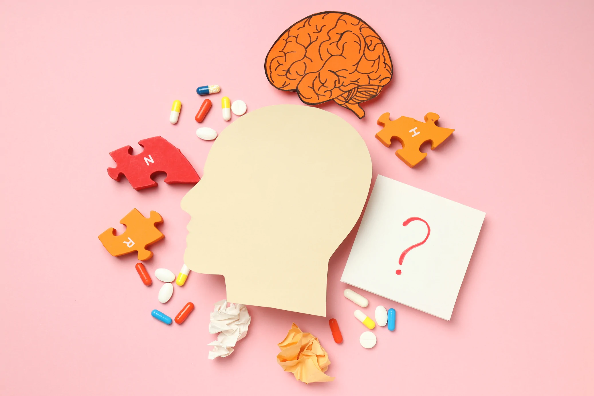 Silhouette of a head with puzzle pieces, pills, brain art, question mark card, and crumpled paper on pink—reflecting Always Reddy Nutrition in Pittsburgh, PA led by dietitian Allison Reddy. in Pennsylvania