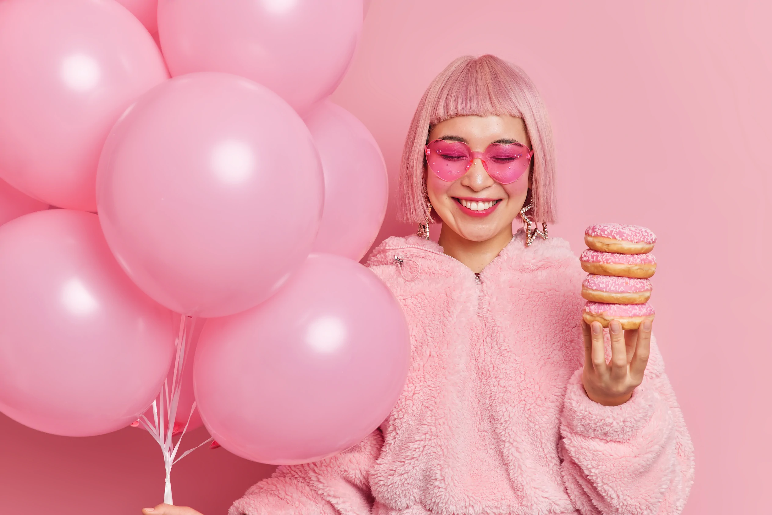 Person in a pink outfit and glasses with pink balloons and donuts stands before a pink background, representing Always Reddy Nutrition in Pittsburgh, PA, owned by dietitian Allison Reddy. in Pennsylvania