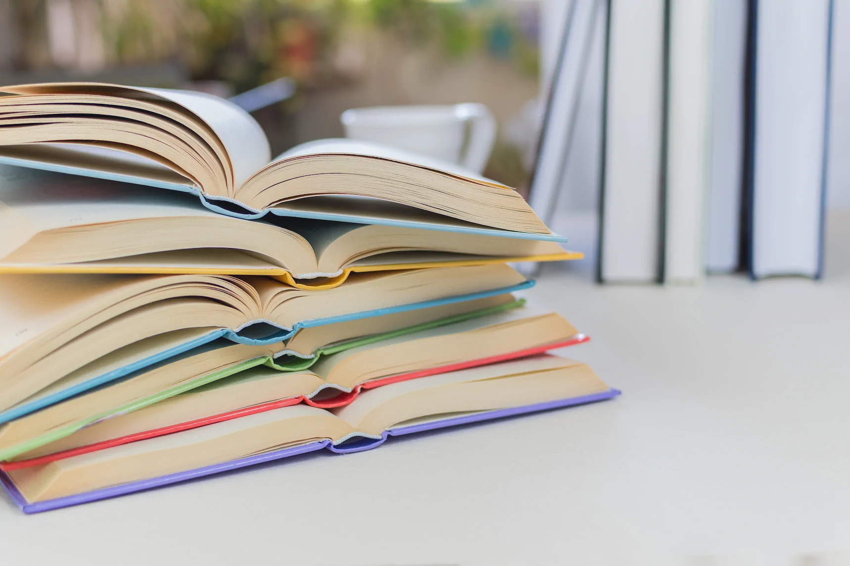 A stack of five open books with colorful covers sits on a white surface at Always Reddy Nutrition in Pittsburgh, PA, owned by dietitian Allison Reddy, specializing in neurodivergent and fertility nutrition. in Pennsylvania