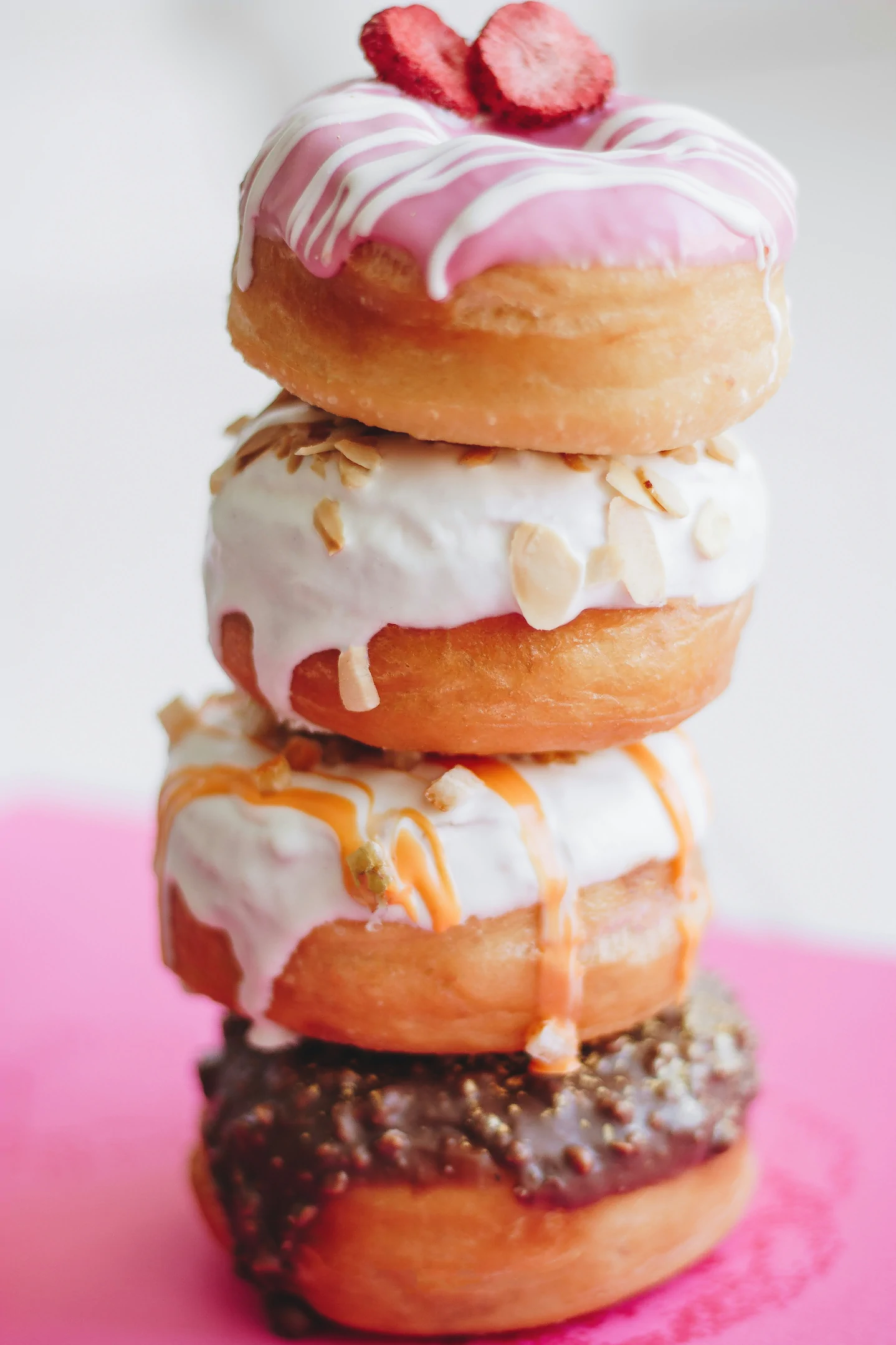 A stack of four decorated donuts with various icings and toppings, arranged on a pink surface at Always Reddy Nutrition in Pittsburgh, PA, owned by dietitian Allison Reddy specializing in diverse nutrition counseling. in Pennsylvania
