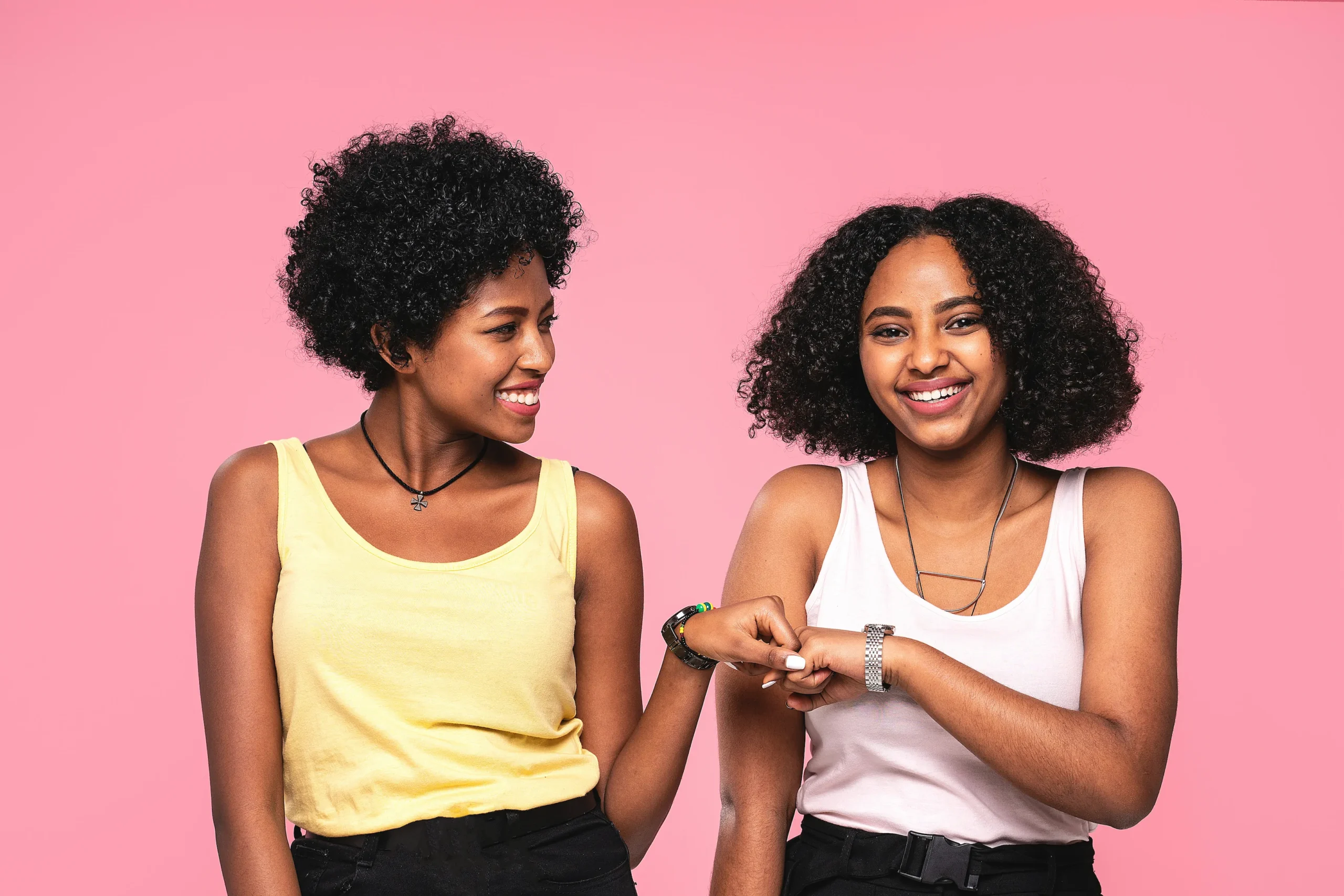 Two young women stand side by side against a pink background, smiling and fist bumping, representing Always Reddy Nutrition in Pittsburgh, PA—owned by dietitian Allison Reddy, specializing in nutrition counseling for neurodivergent individuals, fertility, non-diet nutrition, and eating disorders. in Pennsylvania